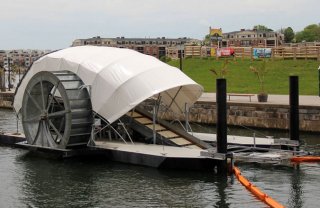 Water wheel on side drives a conveyer belt that pulls floating trash from a portion of the harbor. Boom direct trash to mouth of the conveyer belt. Looks rather like a snail, with conestoga wagon like cover.