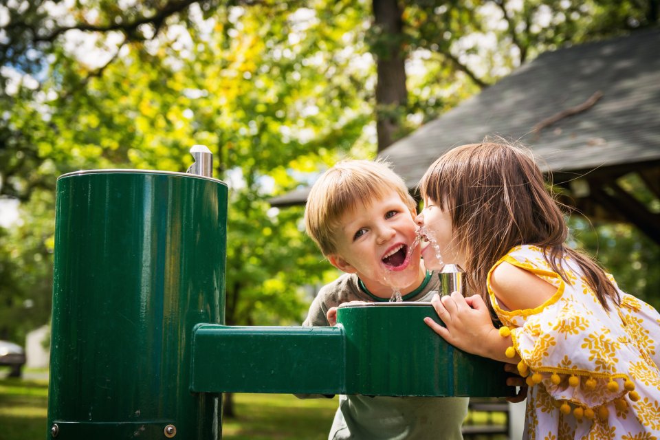 Two kids using a drinking fountain at a park